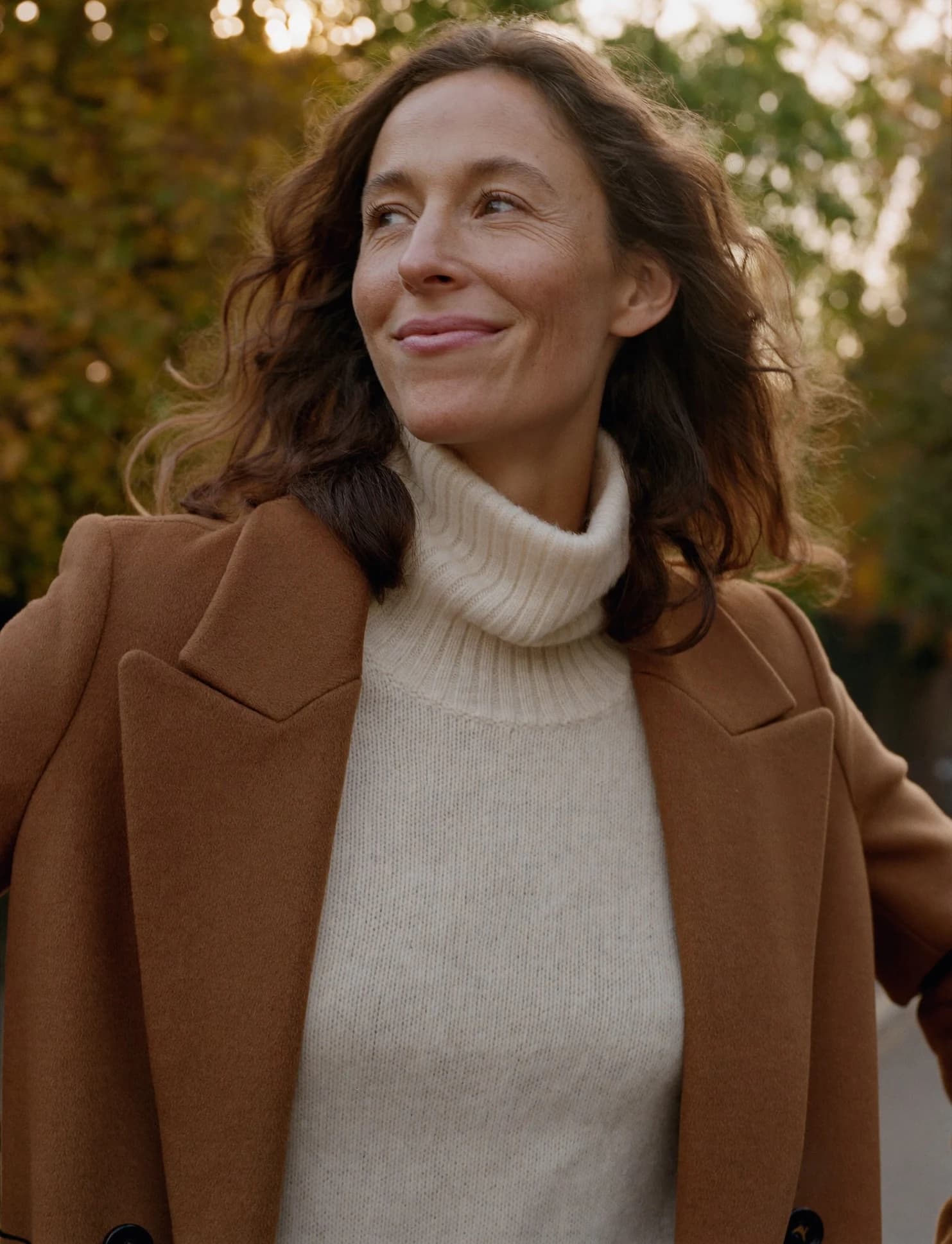 A woman in a camel coat and cream turtleneck walking at golden hour — the calm, restored vitality a NuHealth program is designed to support