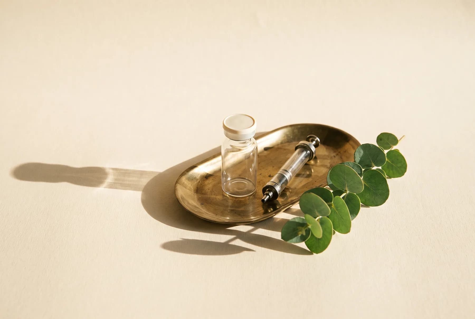 A sealed vial and syringe on a brass tray, prepared for an in-clinic treatment