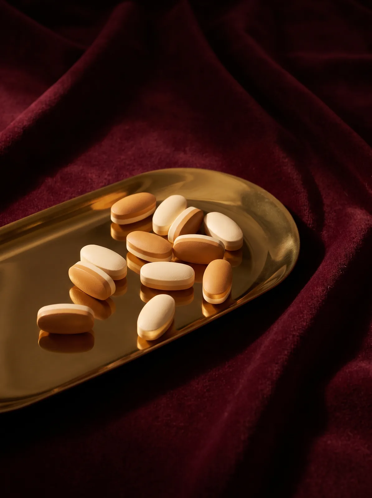 Smooth unmarked tablets on a polished brass tray against deep wine velvet — discreet, premium compounded medicine for sexual health