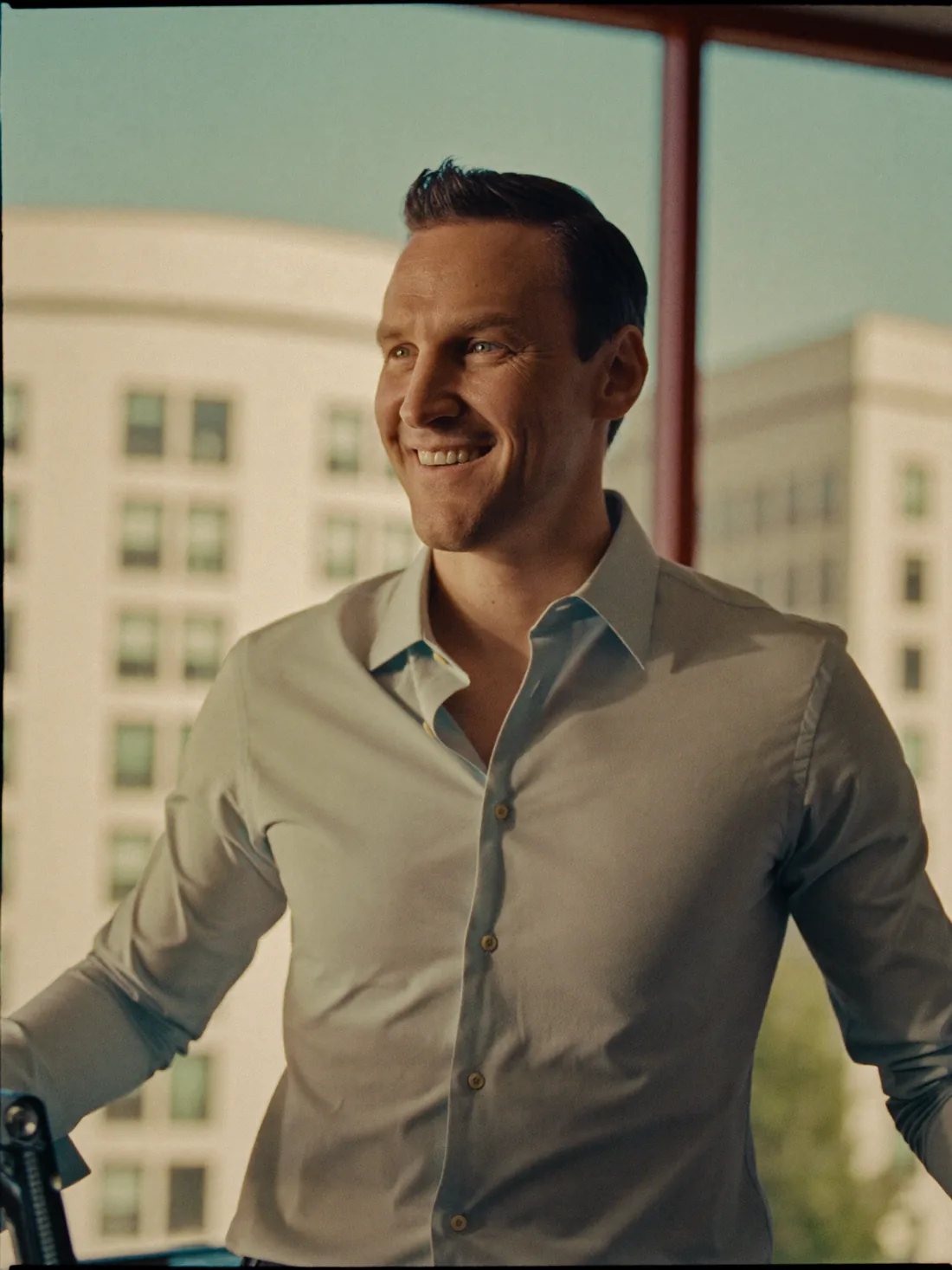 A sharp, confident man in his early forties by an office window in warm light, the clear-headed focus a hormone-optimization program supports
